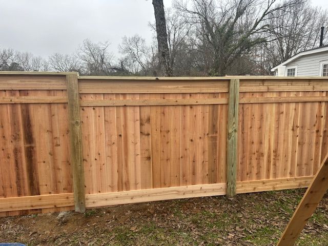 Wooden privacy fence in a yard, built with vertical planks and horizontal rails.