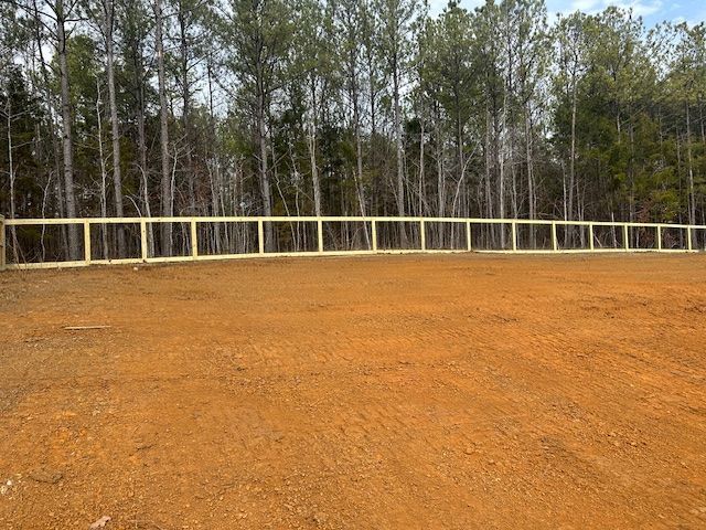 A new wooden fence along the edge of a cleared dirt lot in front of a line of trees.