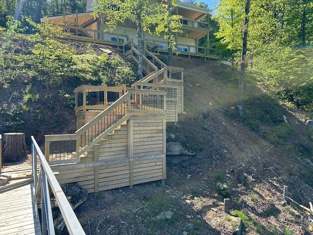 Wooden staircase leading up a hill to a multi-level house, overlooking a lake.