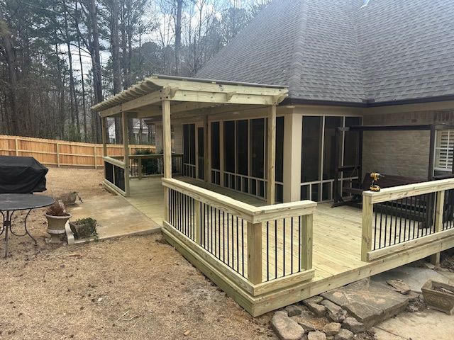 A wooden deck and screened porch extend from a house. Railing, gravel, and a fence are also visible.