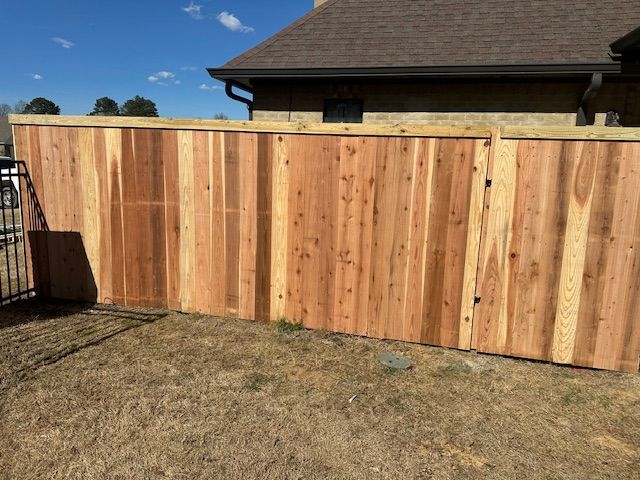 Wooden privacy fence in a backyard, beside a house with a brown roof and brown grass.