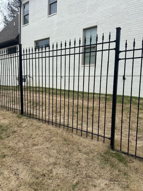 Black metal fence in front of a white brick building with a brown, grassy yard.