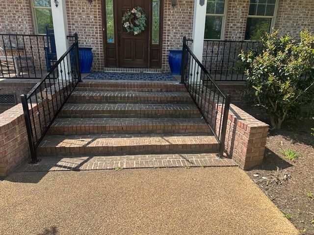 Brick steps with black metal handrails leading to a front door with a wreath.