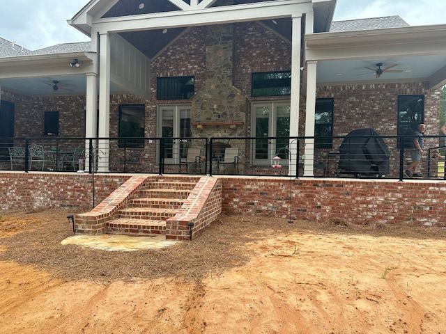 Brick house exterior with a porch, steps, and black railing.