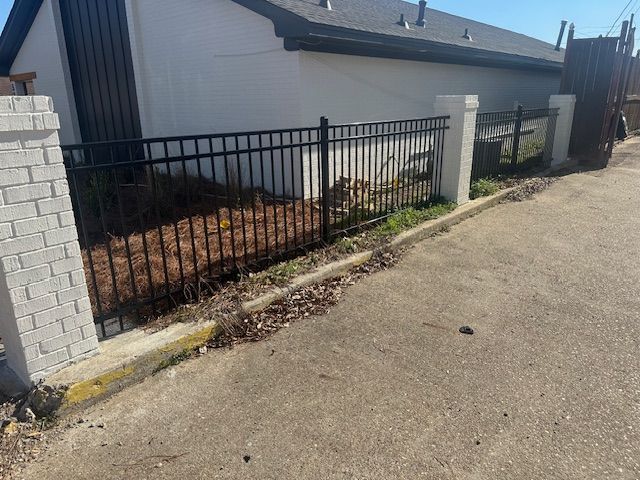 Black metal fence along a building, bordered by a concrete curb and asphalt.
