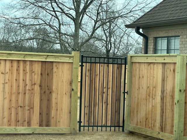Wooden fence with black metal gate in front of a brick building.
