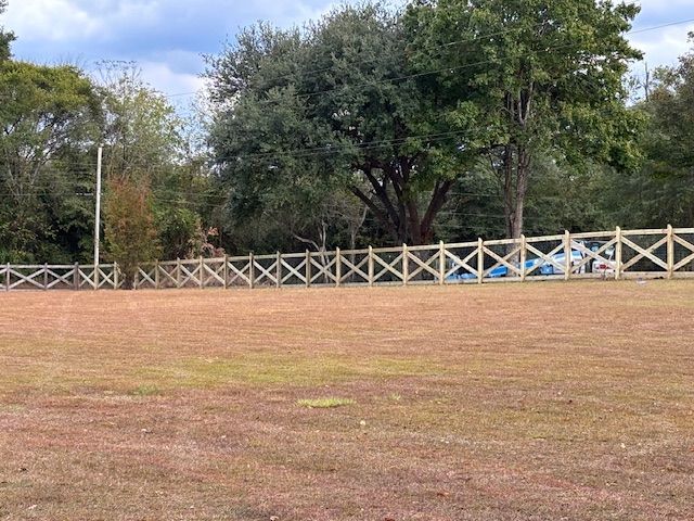 Lawn with a newly built wooden fence. Large tree and other trees in the background. Overcast sky.