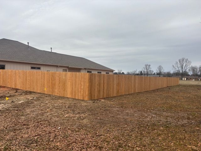 Wooden privacy fence surrounding a grassy yard next to a house under a cloudy sky.