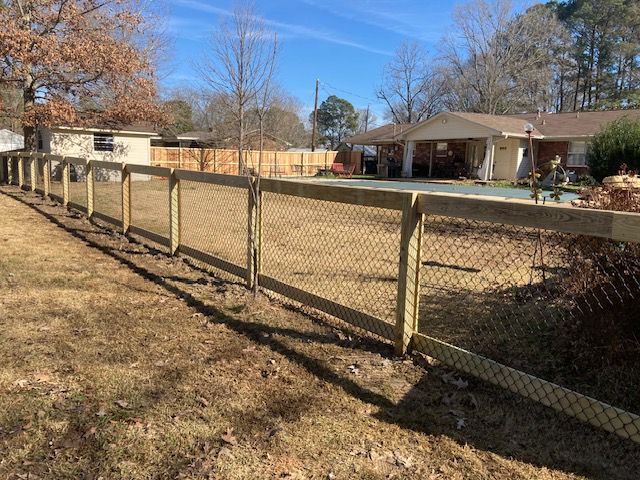 Wooden fence with chain link against a yard and a house under a blue sky.