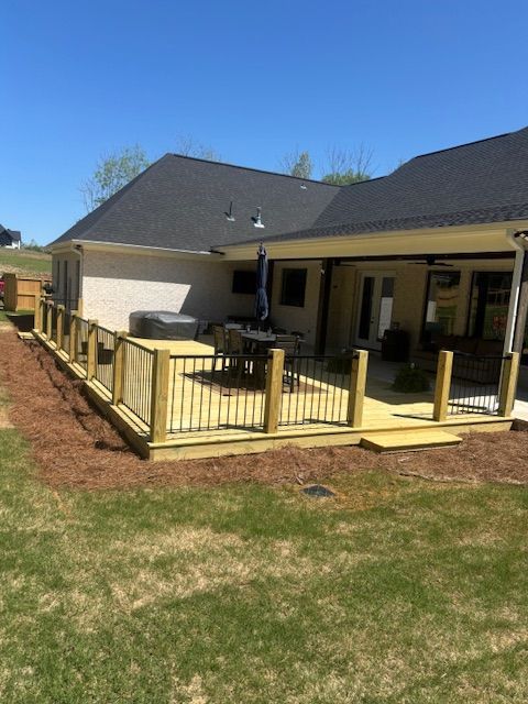 Wooden deck with black railings and light wood posts next to a house with a black roof.