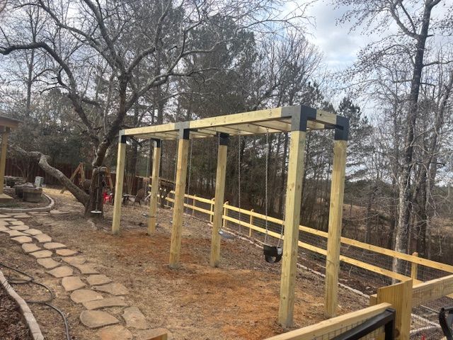 Wooden swing set in a yard, near a stone pathway and a wooden fence. Overcast day.