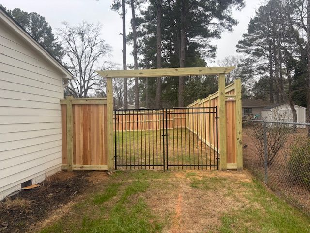 Wooden fence with arched top, black gate, and short grass pathway in backyard setting.