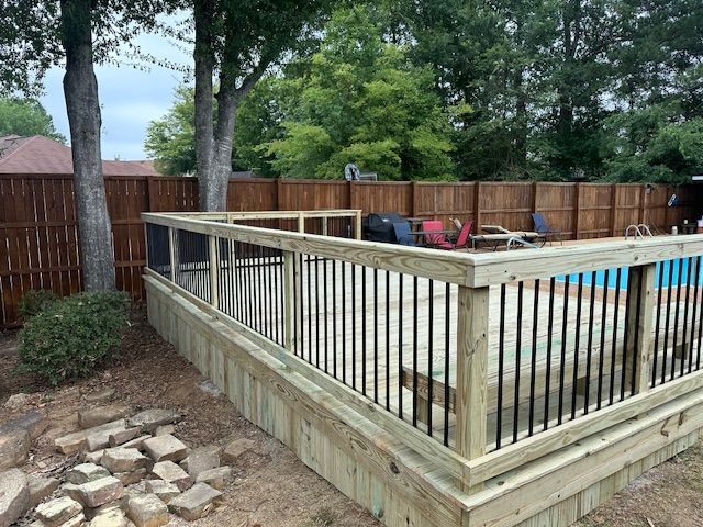 Wooden pool deck with black railing and brown privacy fence in the background.