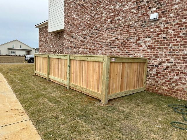 Wooden fence enclosure against a brick building on a grassy lawn.
