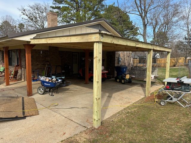 A newly built wooden carport attached to a brick home. Tools and equipment are scattered around.