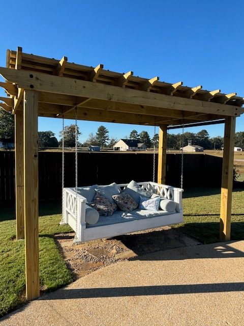 Wooden pergola with hanging swing bed, blue cushions, in a yard.