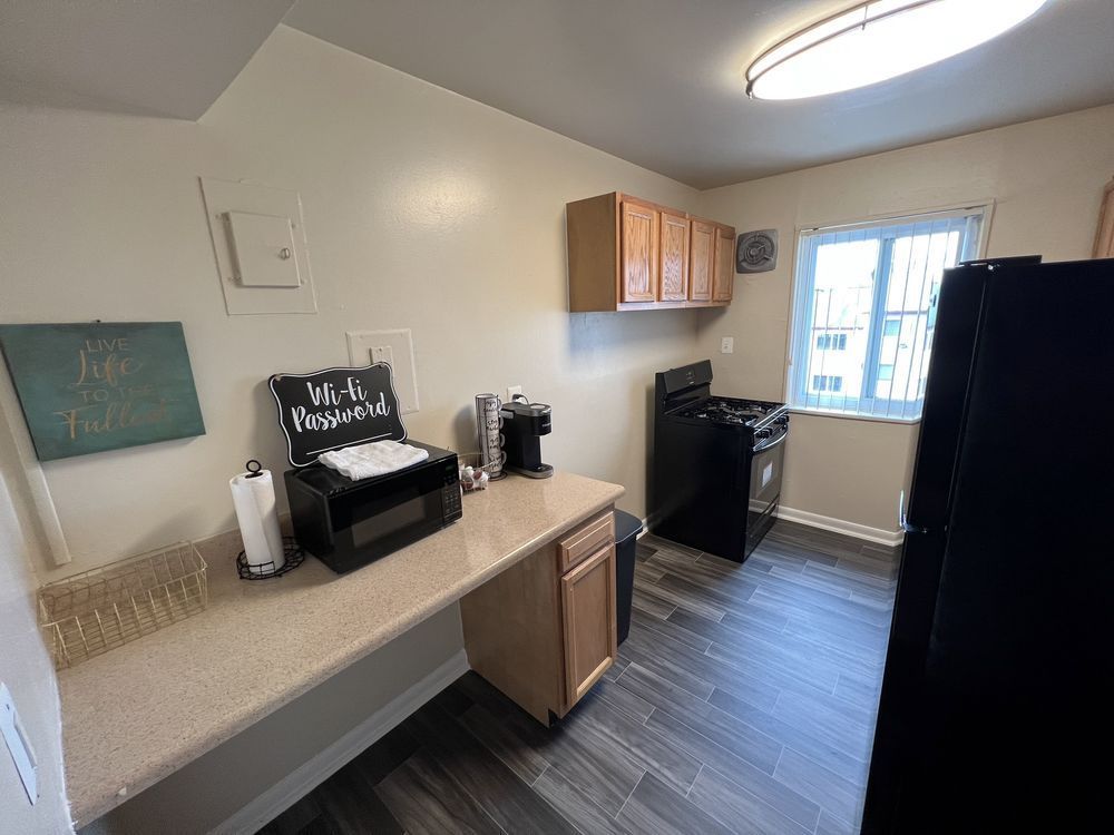 Kitchen with a countertop, cabinets, stove, microwave, and window. Walls are light-colored, with dark wooden floors.