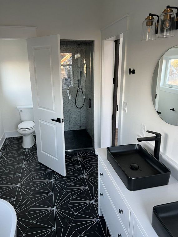 Bathroom with patterned black and white floor tiles, black sink and faucet, shower with glass door, and white cabinetry.