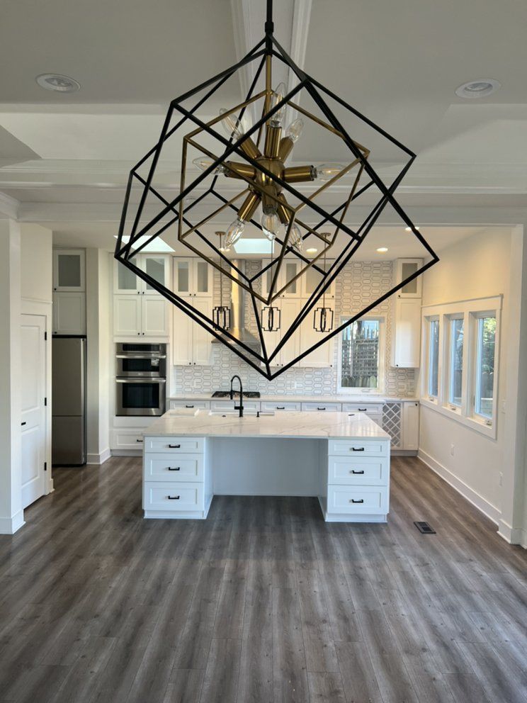Modern kitchen with white cabinets, gray flooring, and a large geometric black and gold chandelier above a white island.