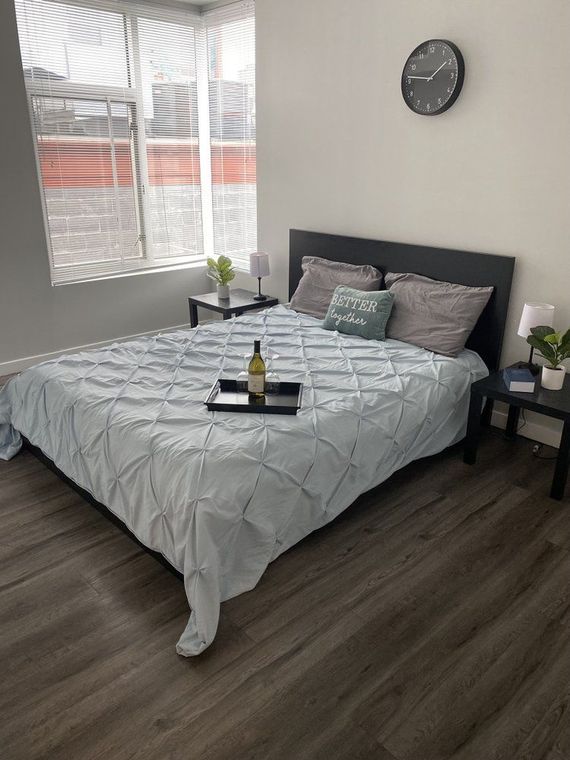 Bedroom with a bed, nightstands, and a window. Bed has blue quilted comforter, pillows, and a tray with a bottle.