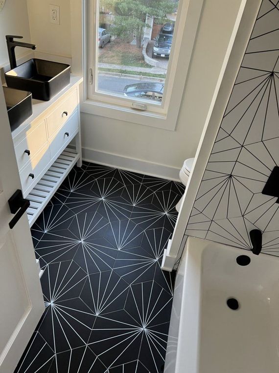 Black and white bathroom with geometric floor tiles, a white vanity with a black sink, and a bathtub.