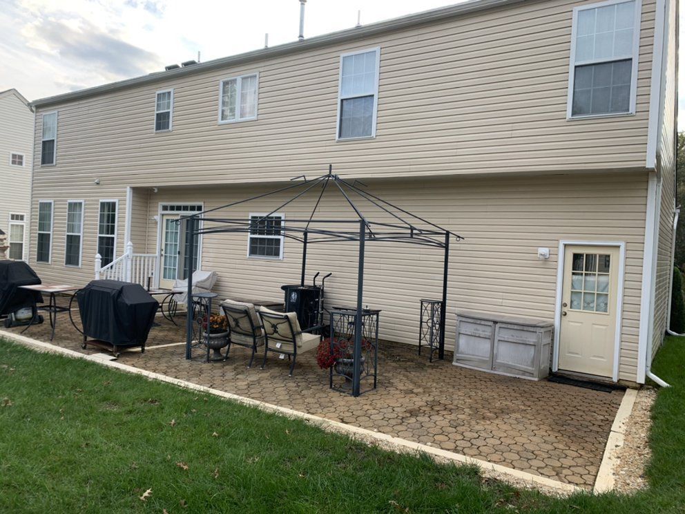 Backyard patio with furniture, grill, and a gazebo structure in front of a two-story beige house.