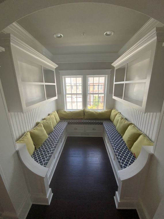 A built-in seating nook with storage and window, featuring white trim, blue patterned cushions, and yellow pillows.