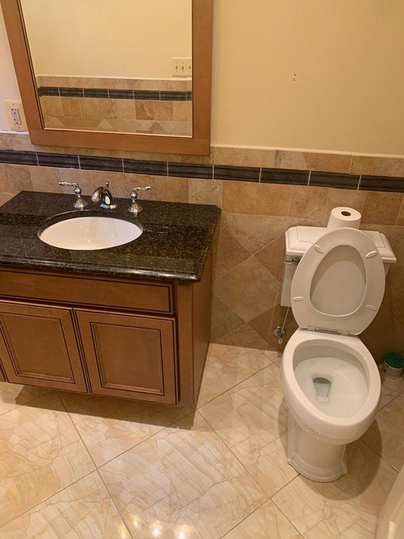 A bathroom with a toilet, vanity, and mirror. The toilet seat is up. The vanity has a dark countertop and brown cabinets.