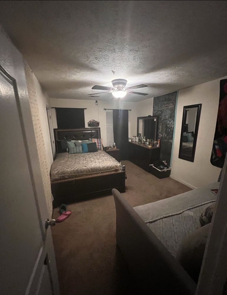 Dark bedroom with a bed, dresser, mirror, and sofa. Brown carpet and walls.