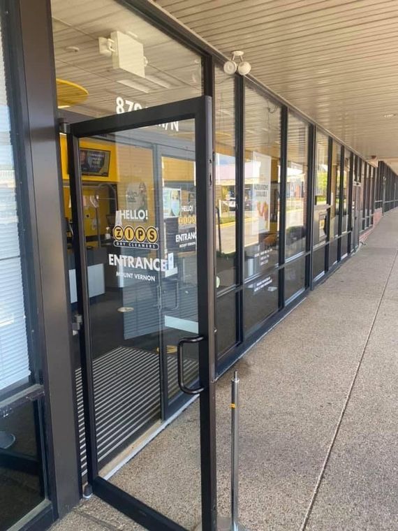 Open glass door of a storefront with a yellow and black sign. Exterior shot on a concrete walkway.