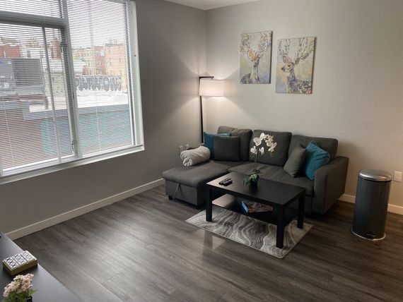 A gray sectional sofa in a living room with wood-look floors, window, art, and a lamp.