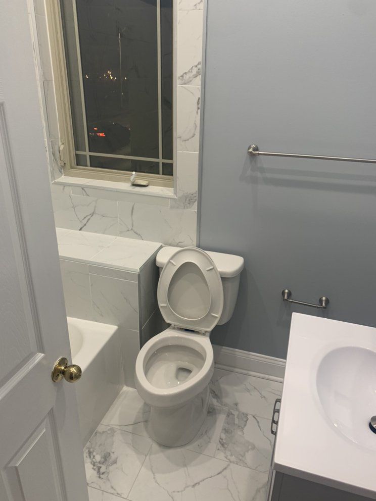 Bathroom with a white toilet, marble-look tile, and a blue wall. The toilet seat is open.