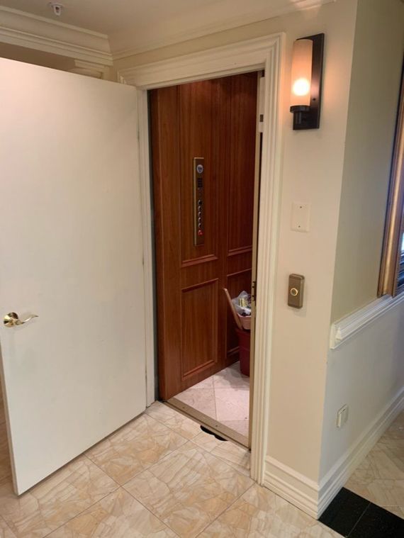 An open doorway reveals a wood-paneled elevator. A white door is ajar on the left. A light fixture is to the right.