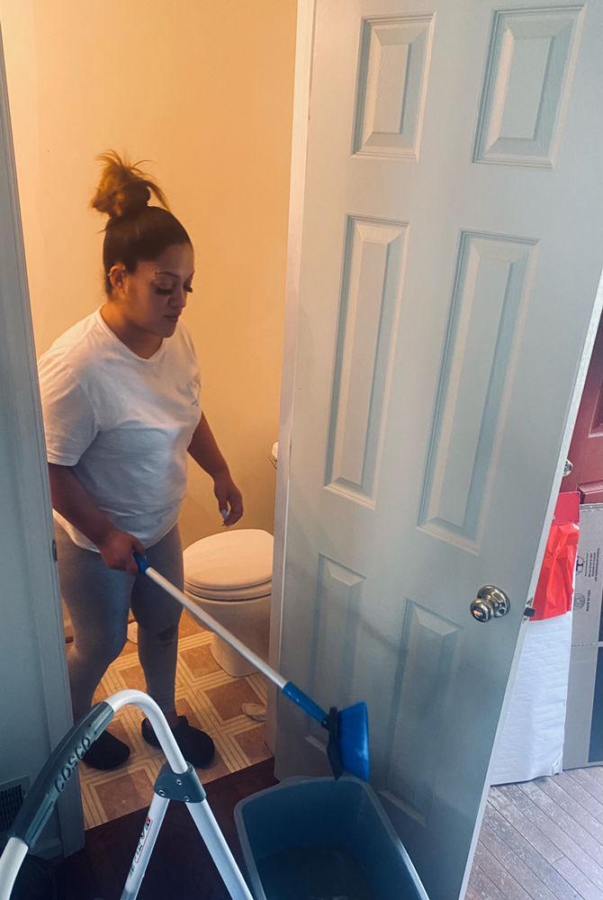 Woman cleaning a white door with a long-handled cleaning tool. She's standing near a toilet and a step stool inside a room.