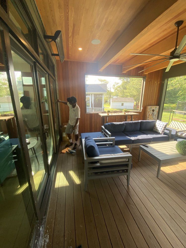 An outdoor living area with a young person standing near a sliding glass door.  There are blue couches and a wooden ceiling.