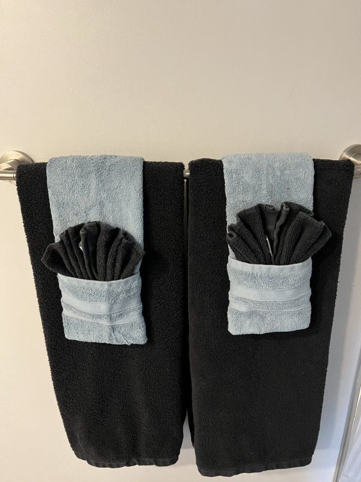 Two black towels hanging on a bar, each with a folded black hand towel tucked into a light blue folded pocket.