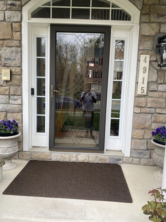 A house front door with a screen door, address 4915, and stone exterior walls. There are potted flowers and a doormat.