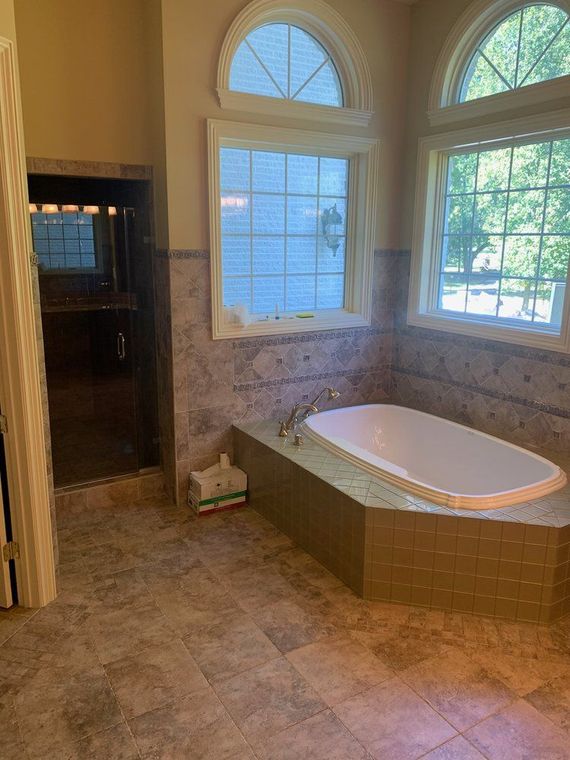 Bathroom with a built-in tub, shower, and windows. The walls are tiled, and natural light streams through the arched windows.