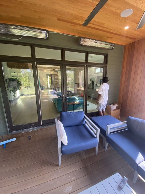 Outdoor patio with blue furniture and person standing near glass doors, wooden deck and ceiling.
