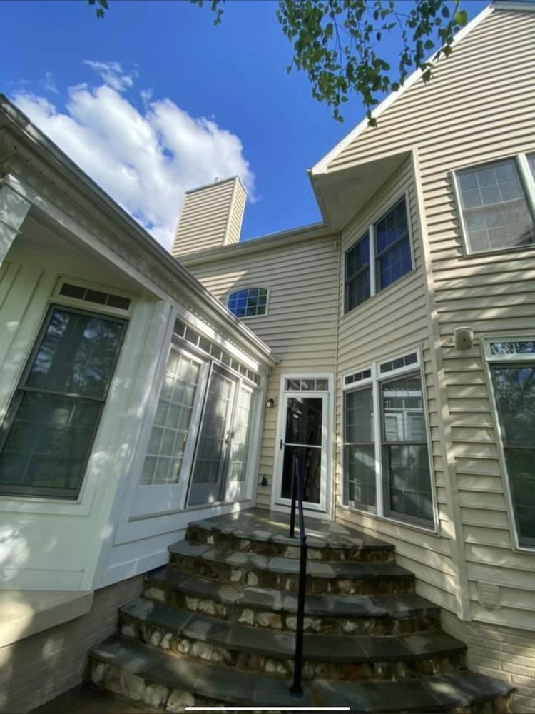 A house with stone steps leading to a doorway. The house is tan with white trim, and the sky is blue with clouds.