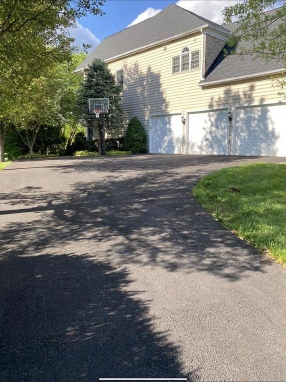 Driveway leading to a two-story house with a basketball hoop, and two garage doors, on a sunny day.