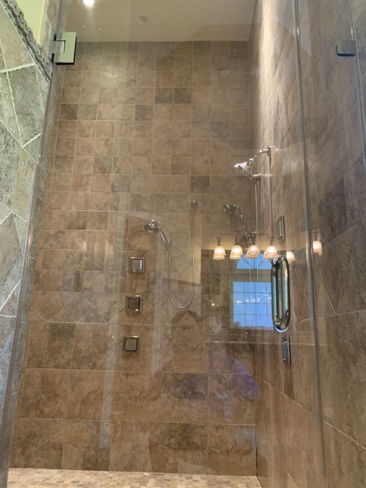 A tall, tiled shower with glass doors and multiple showerheads; the space is brown and has silver fixtures.