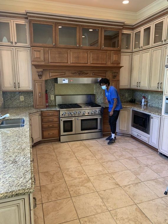 Person wearing a face mask in a spacious kitchen with stainless steel appliances and light-colored cabinets.