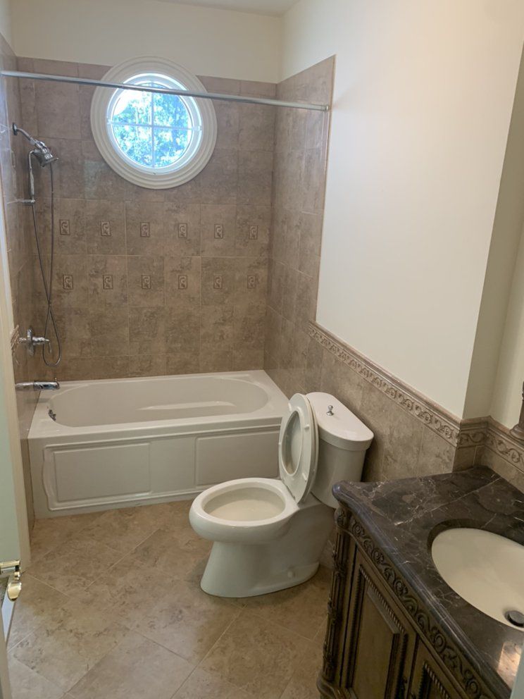 Bathroom with a white tub, toilet, and vanity with a brown countertop. Beige tiled walls and floor.