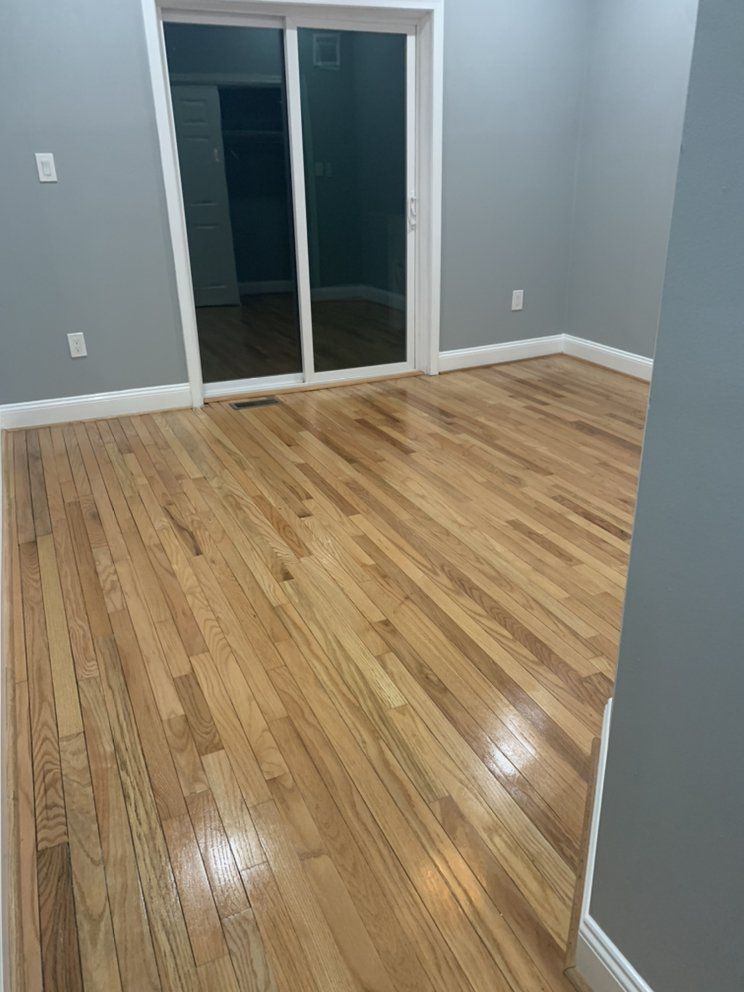 Empty room with hardwood floors, gray walls, and a sliding glass door. White trim and baseboards are visible.