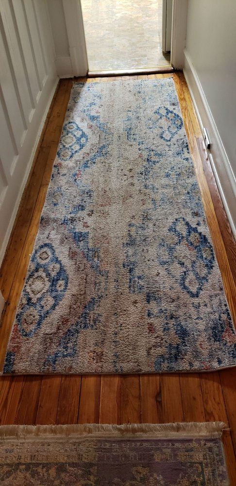 A long, blue and cream patterned rug runs down a wooden hallway. A doorway is at the end.