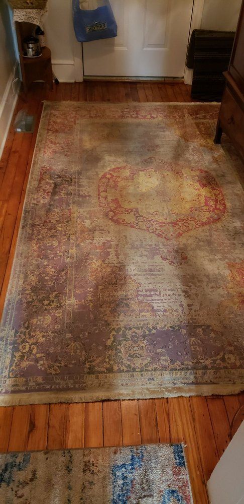 A rectangular, distressed rug with red, brown, and yellow accents sits on a wooden floor.