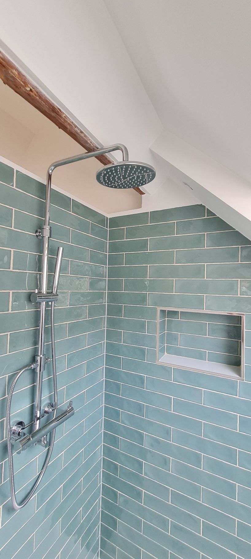 Een douche met blauwgroene, baksteenachtige tegels, een ingebouwde plank en een chromen douchekop.