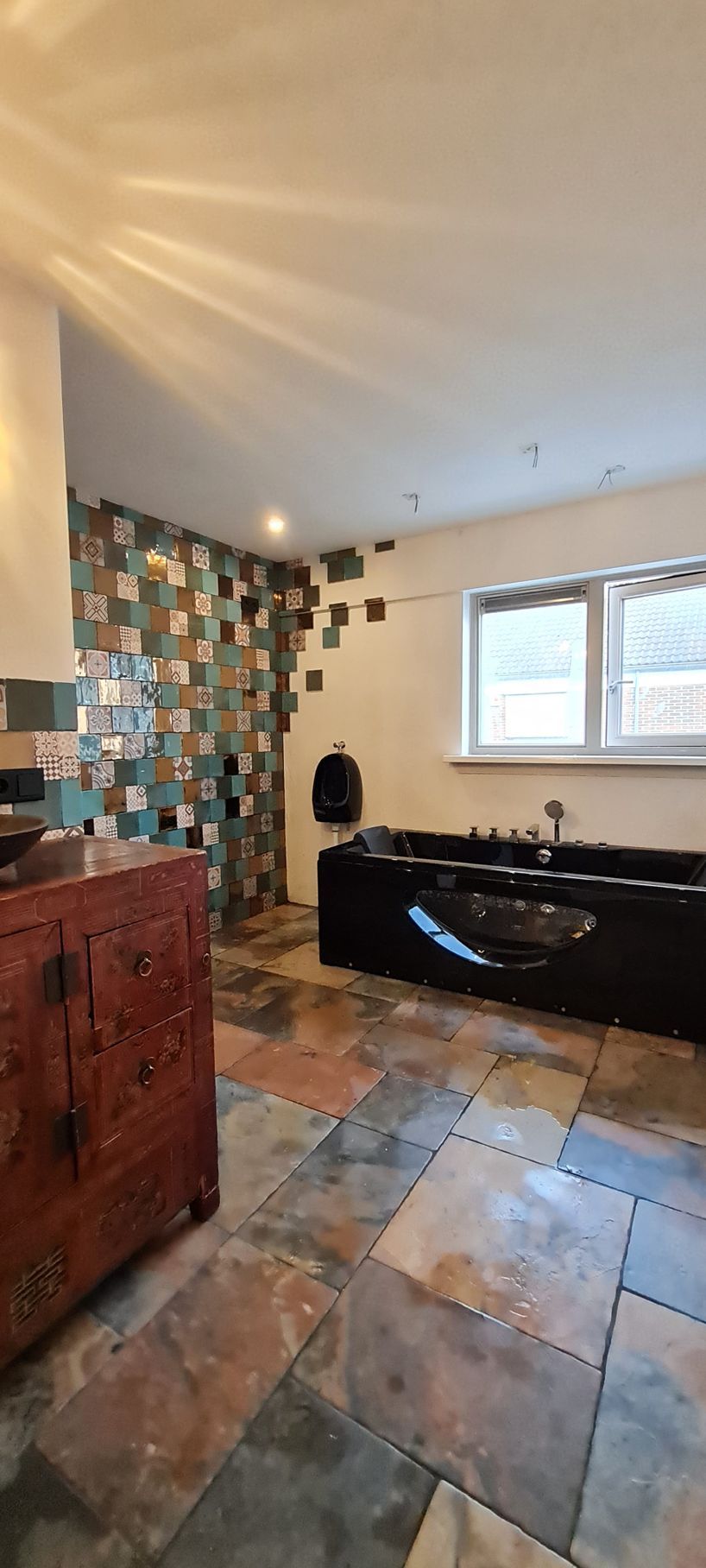 Badkamer met een zwart bad, betegelde vloer en kleurrijke accentmuur.