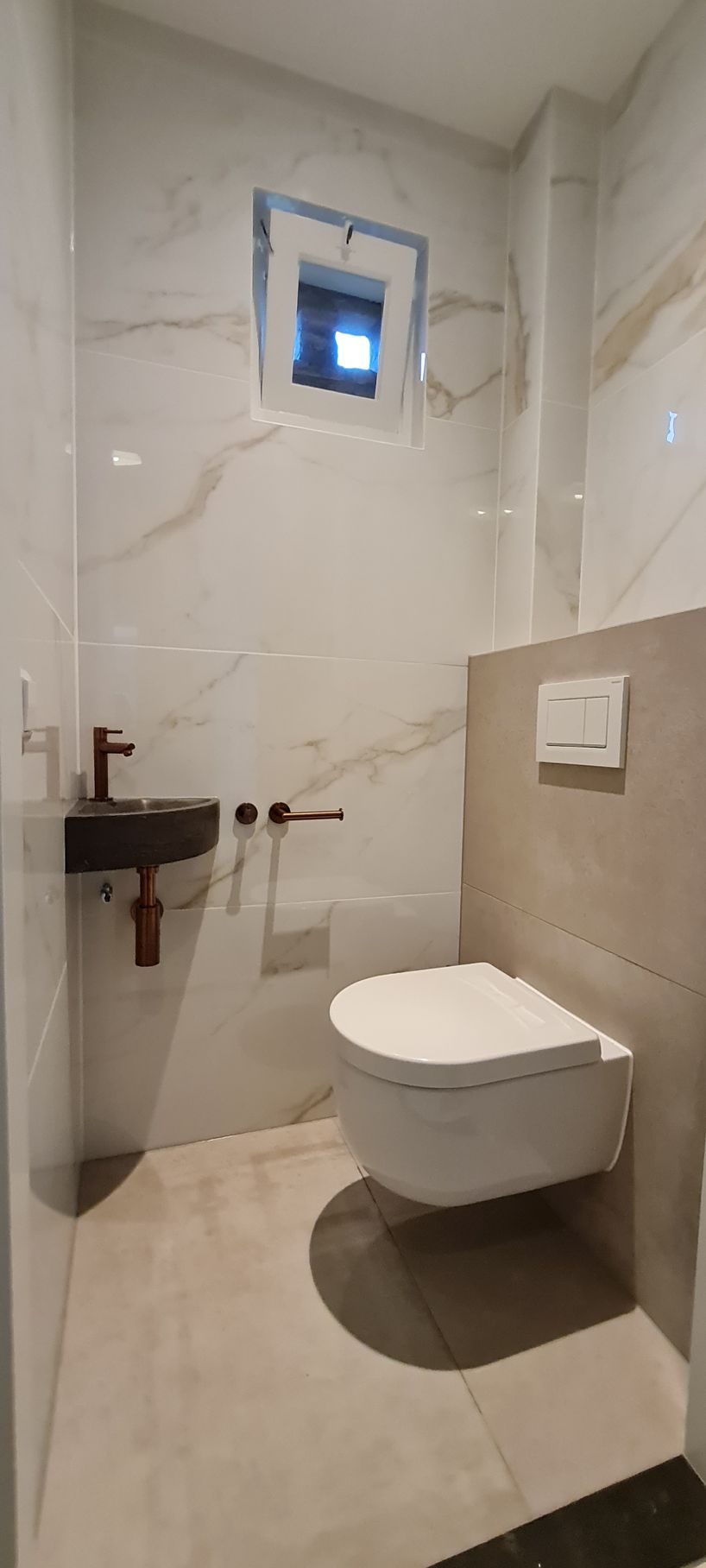 Kleine, moderne badkamer met muren met marmerlook, een zwevend toilet en een kleine wastafel.
